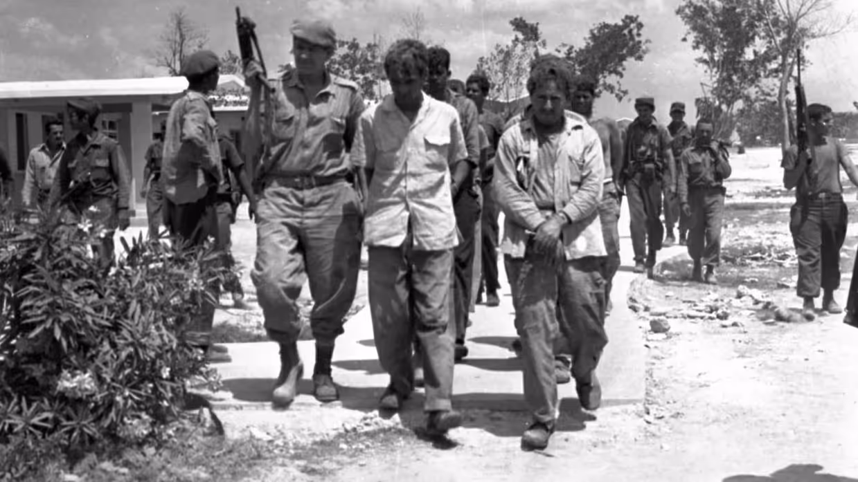 Gevangenen in uniform worden afgevoerd door bewapende soldaten. 