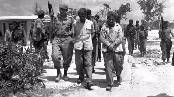 Gevangenen in uniform worden afgevoerd door bewapende soldaten. 