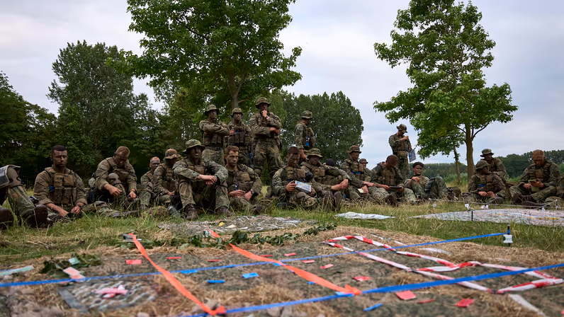 Mariniers zitten in het gras en bekijken een geïmproviseerde maquette.