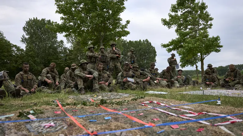 Mariniers zitten in het gras en bekijken een geïmproviseerde maquette.