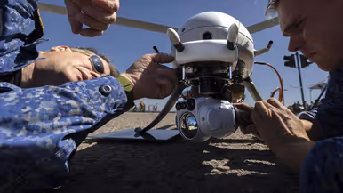 Twee mannen sleutelen aan een drone en liggen op de grond.