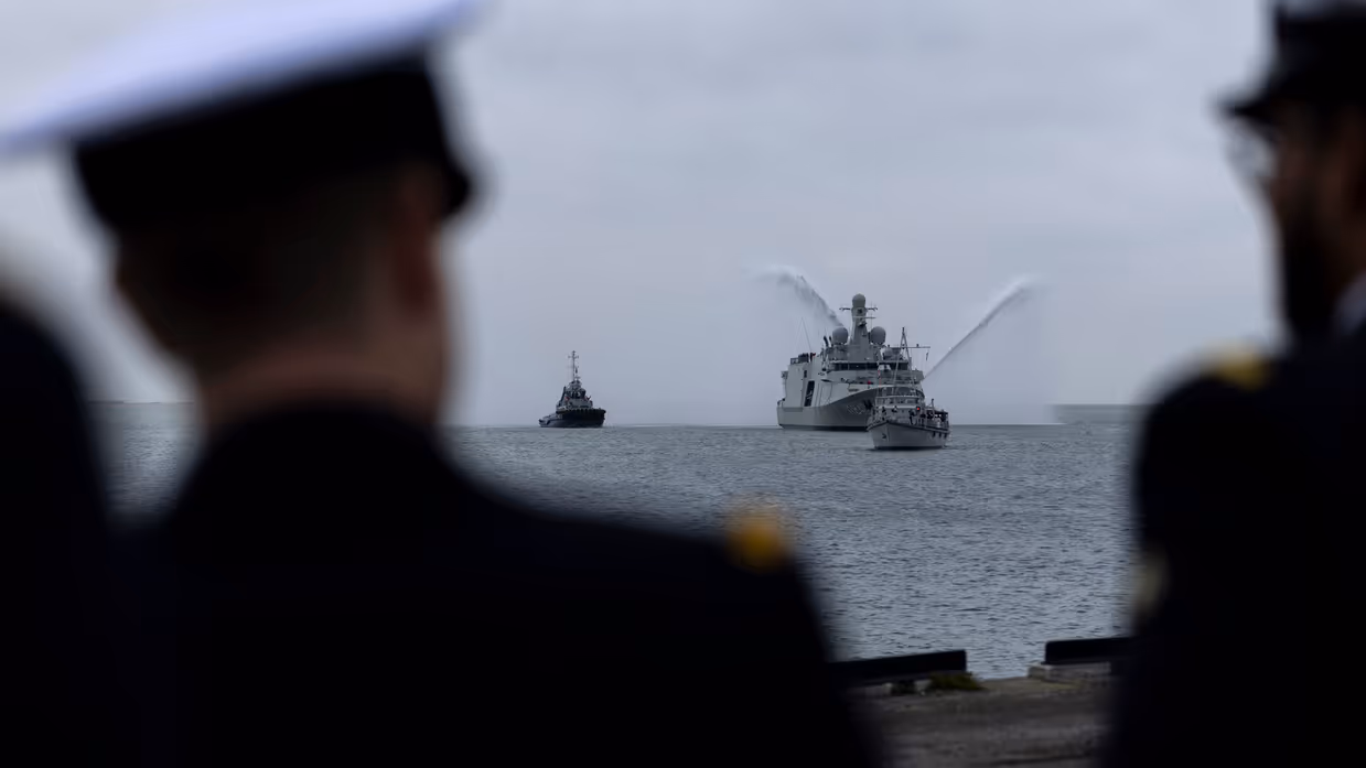 Marineschip de ‘Vlissingen’ op zee, daarnaast twee sleepboten die met hun waterkanonnen spuiten. Het schip wordt voorgegaan door een kleine mijnenveger. Op de tweede afbeelding hetzelfde schip, maar dan gezien langs een tweetal marineofficieren aan de wal. 
