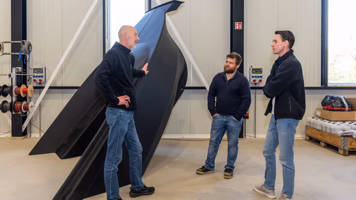 Drie mensen in fabriekshal in gesprek bij een onderdeel van 3D-geprinte boot.