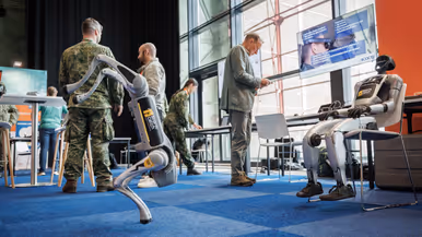 Een lopende en zittende robot met vier personen op de achtergrond.