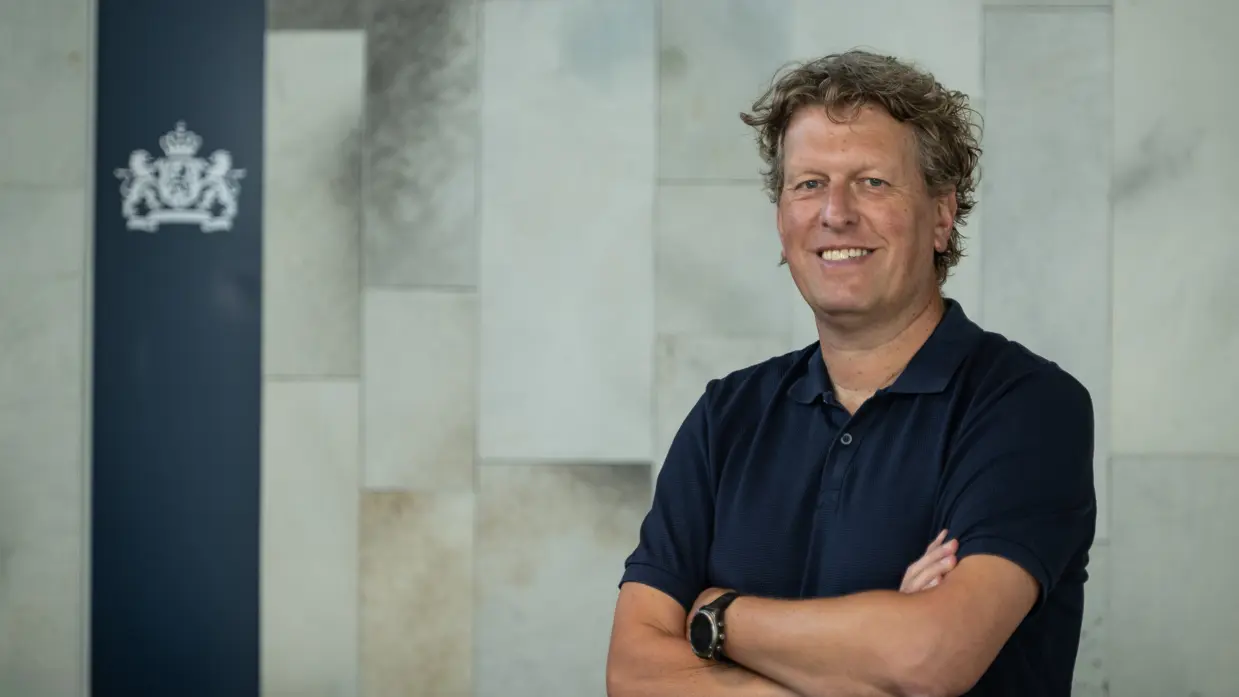 Man met krullen en een blauw poloshirt aan poseert met armen over elkaar. 