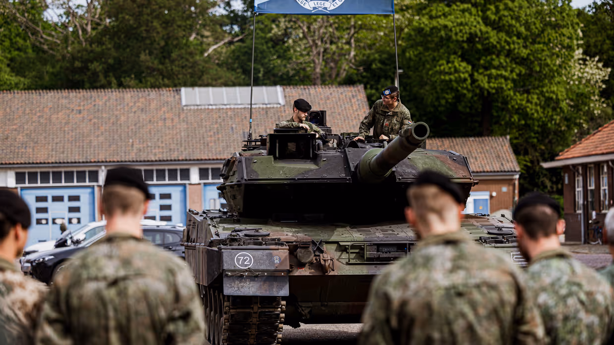 Een Leopard 2A8-gevechtstank met daarop 2 militairen tijdens een ceremonie. Ervoor staan militairen die het voertuig aanschouwen.