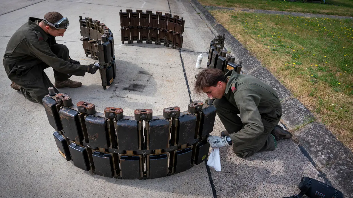 Twee militairen zijn aan het poetsen aan een zware, metalen structuur.