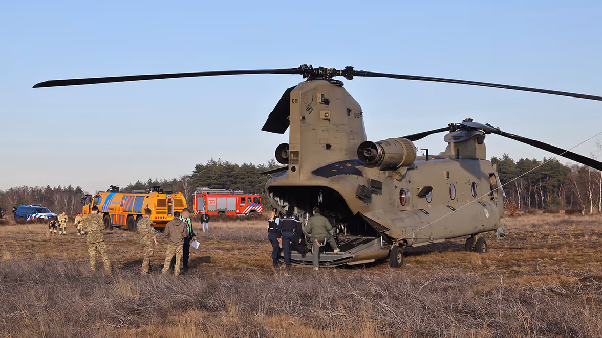 Een militaire helikopter staat in een veld, met daar omheen veel mensen en een gele brandweerauto.