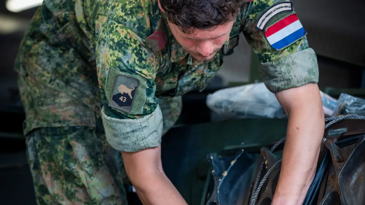 Een militair in overall inspecteert een stuk metaal.