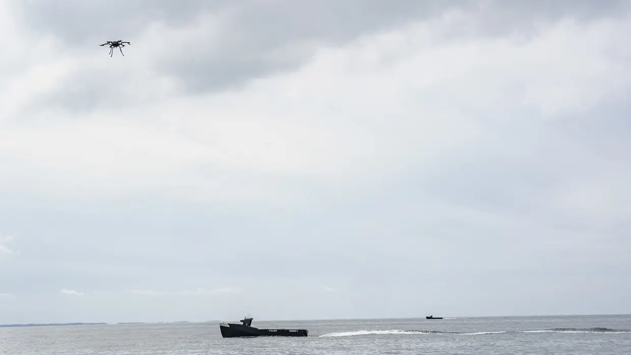 Een drone vliegt boven een kleine onbemande boot.