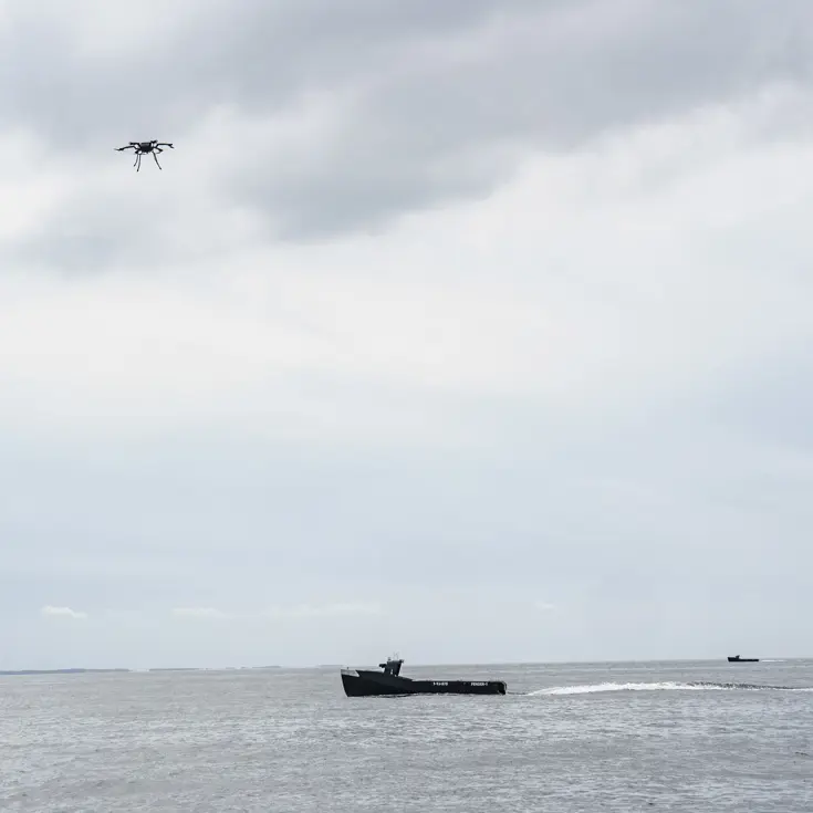 Een drone vliegt boven een kleine onbemande boot.