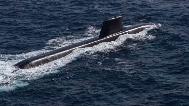Een zwarte, stroomlijnvormige onderzeeboot vaart door golvend, donkerblauw zeewater, met witte golven achter de romp en een kleine toren bovenop. 