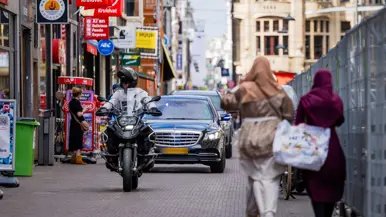 Marechaussee op een motor rijdt voor een aantal zwarte voertuigen uit.