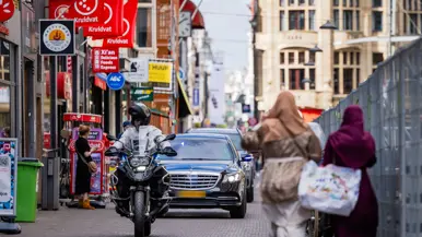 Een motorrijder van de KMar rijdt aan het hoofd van een colonne door een winkelstraat.