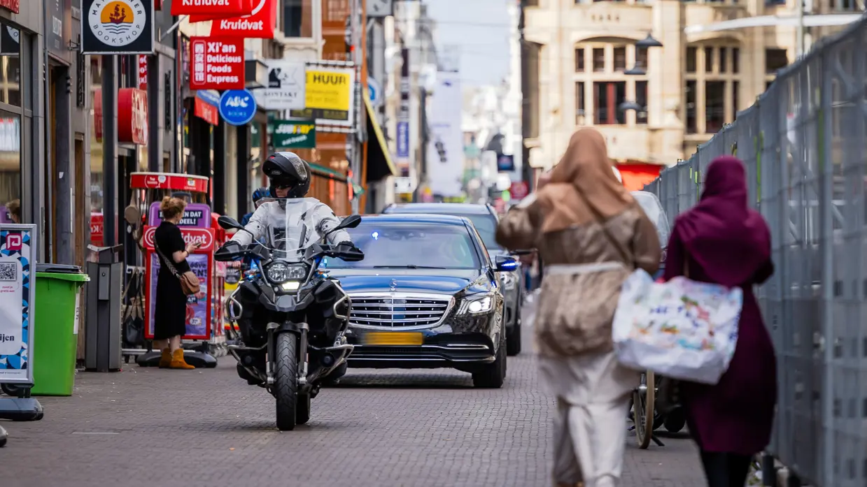 Marechaussee op een motor rijdt voor een aantal zwarte voertuigen uit.