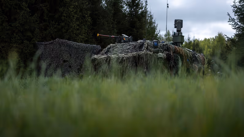 Een stilstaand Fennek-voertuig onder een camouflagenet.