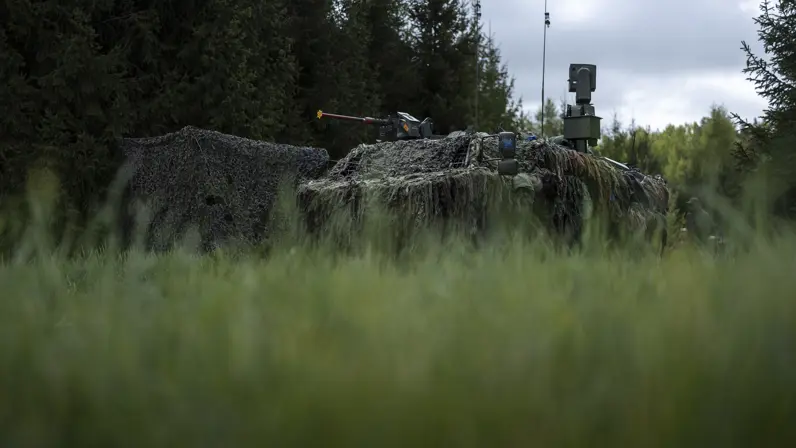 Een stilstaand Fennek-voertuig onder een camouflagenet.