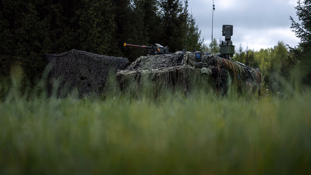 Een stilstaand Fennek-voertuig onder een camouflagenet.