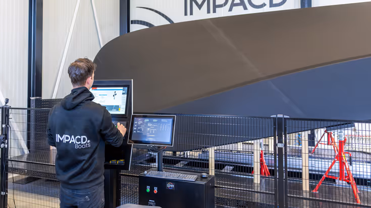  Een medewerker van de botenbouwer staat achter twee computerschermen.