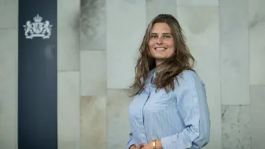Vrouw met lang donkerblond haar en lichtblauw krijtjesoverhemd aan poseert met handen over elkaar.