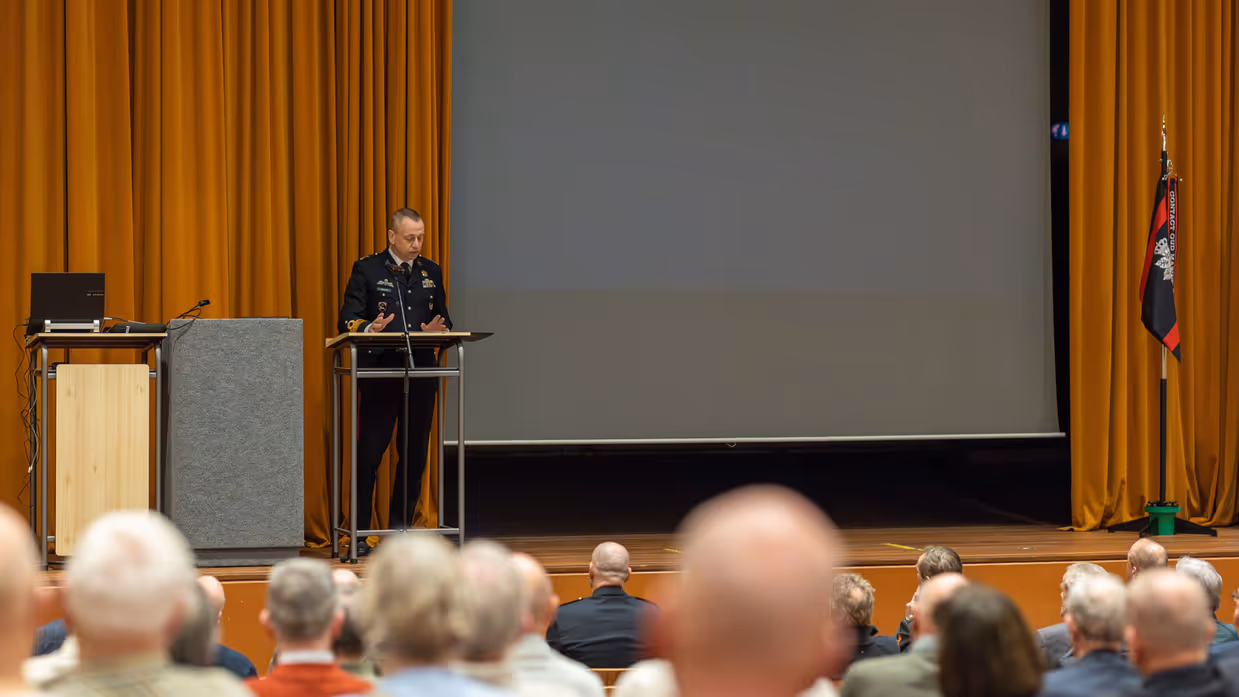 Alttekst: Links: een groep mannen luistert naar een man in uniform op een podium. Rechts: 2 mannen in uniform kijken naar een munt in hun handpalm met drie man om zich heen. 