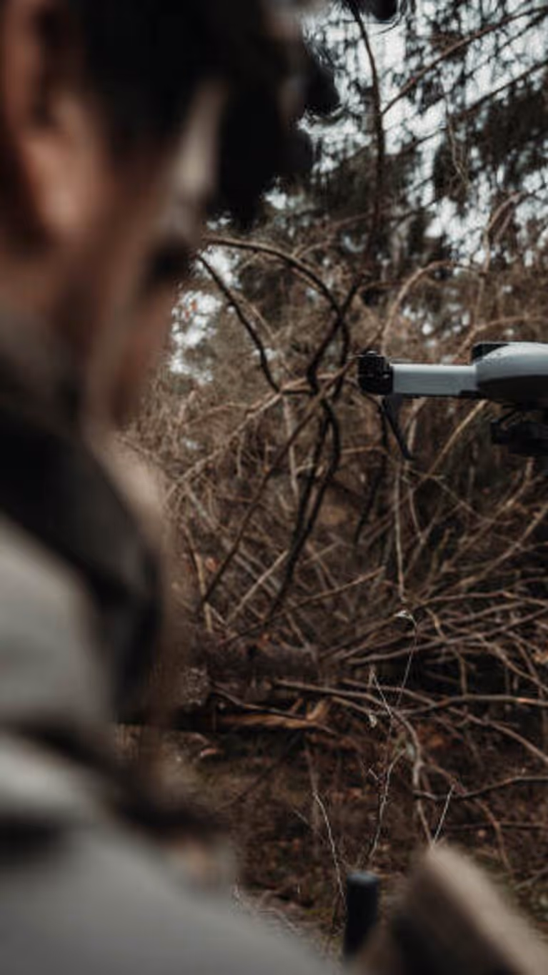 Een grijze drone vliegt voor een militair, die vanaf de achterkant wordt bezien 