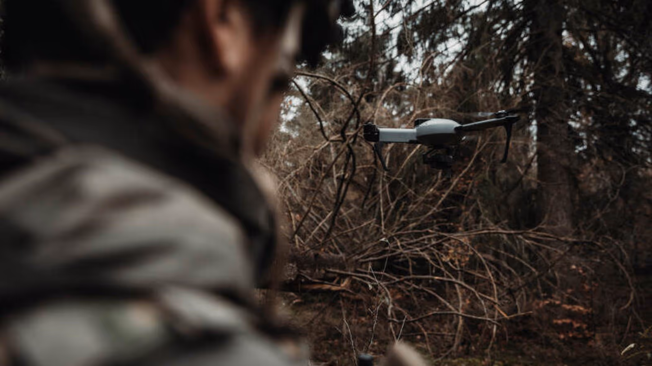 Een grijze drone vliegt voor een militair, die vanaf de achterkant wordt bezien 