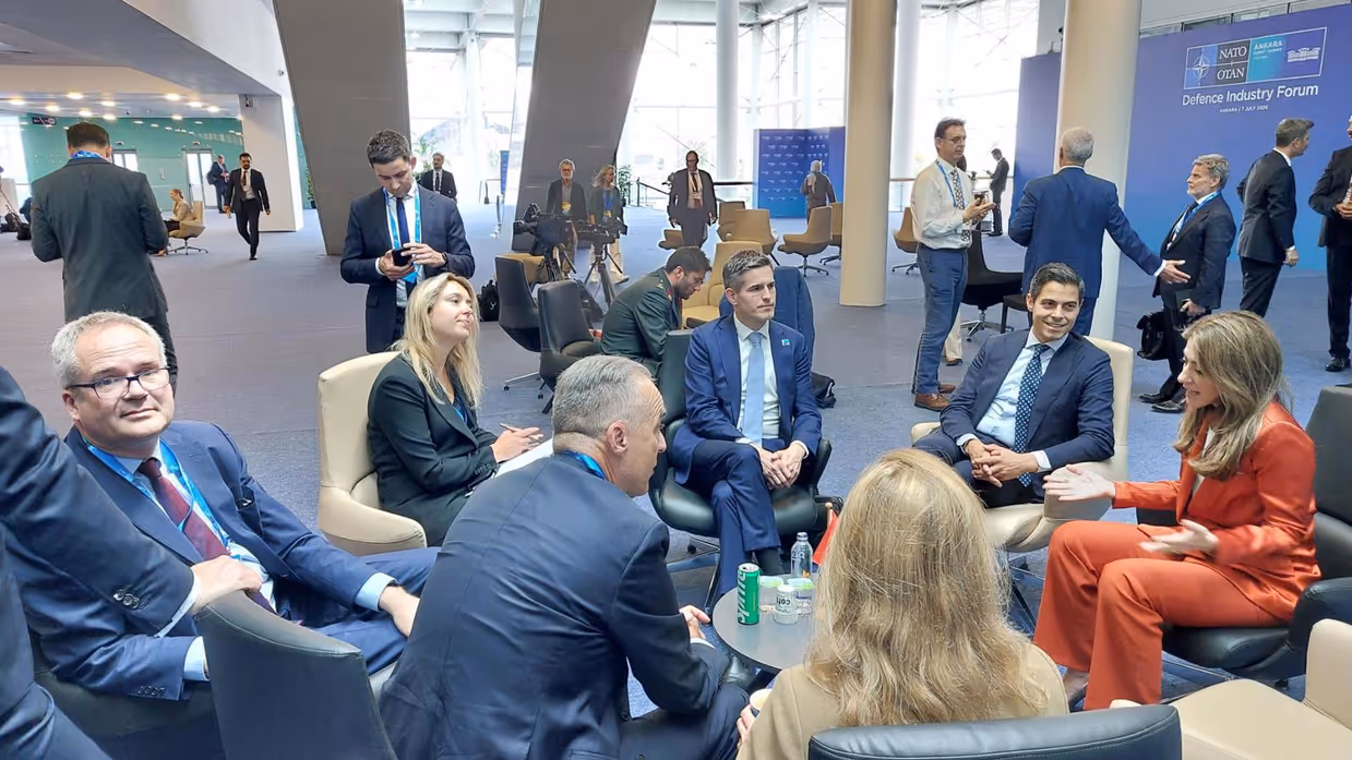 Groepje mensen zit op stoelen in een kring tijdens overleg in conferentieruimte.