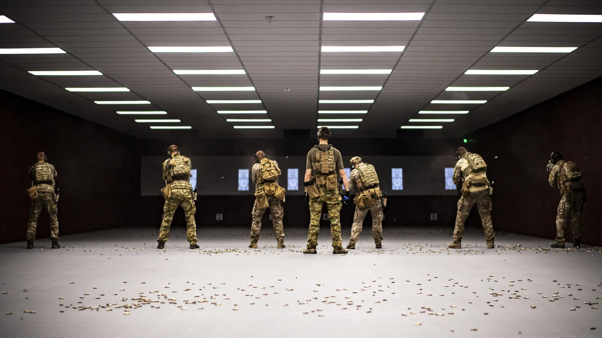 Zes militairen van het KCT, naast elkaar op een overdekte schietbaan. Achter hen ligt de vloer bezaaid met hulzen.