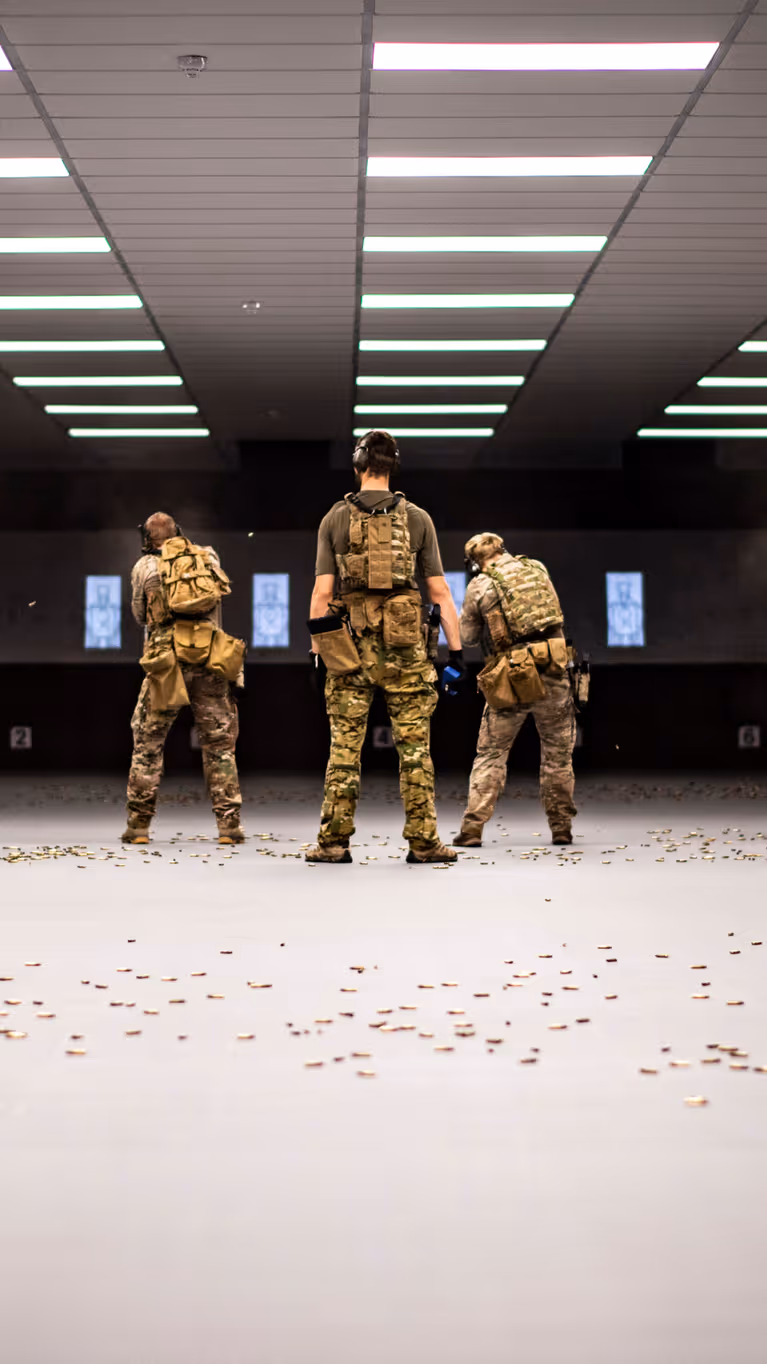 Zes militairen van het KCT, naast elkaar op een overdekte schietbaan. Achter hen ligt de vloer bezaaid met hulzen.