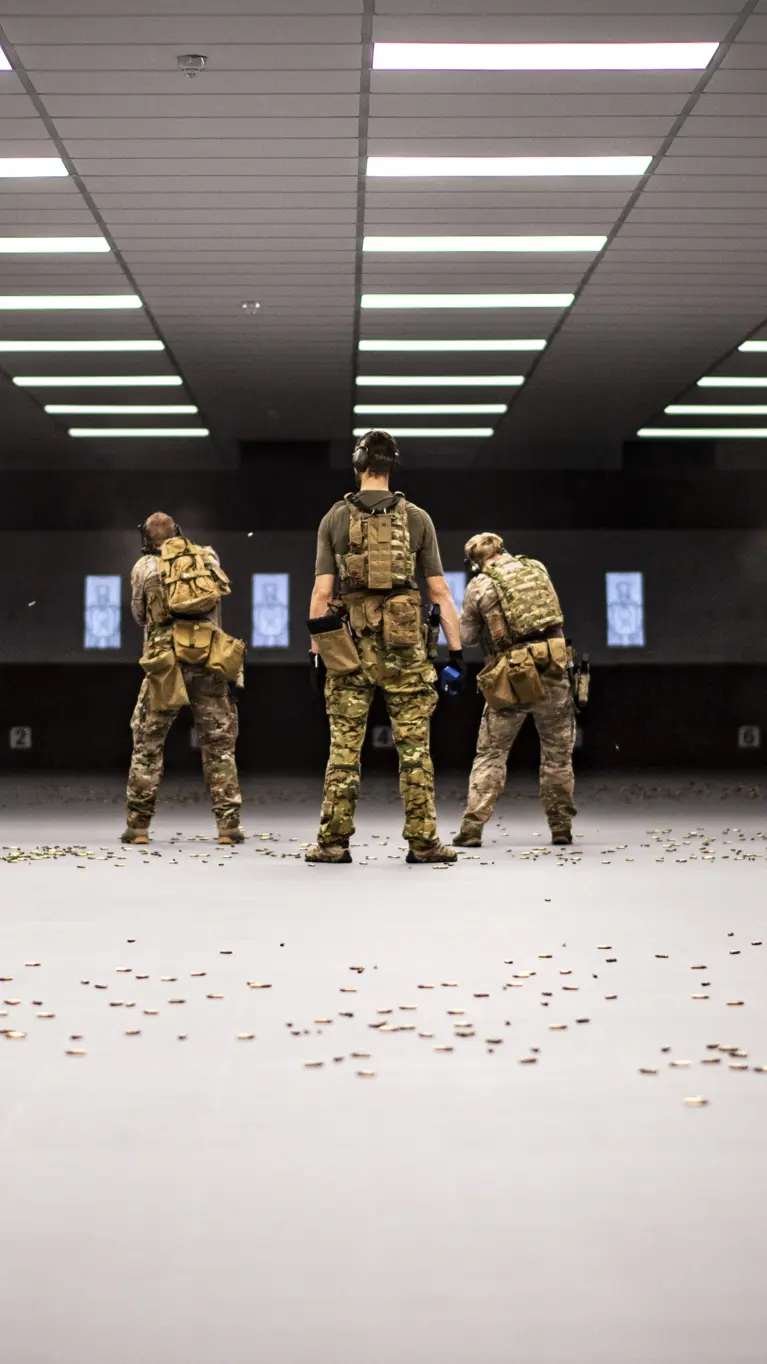 Zes militairen van het KCT, naast elkaar op een overdekte schietbaan. Achter hen ligt de vloer bezaaid met hulzen.