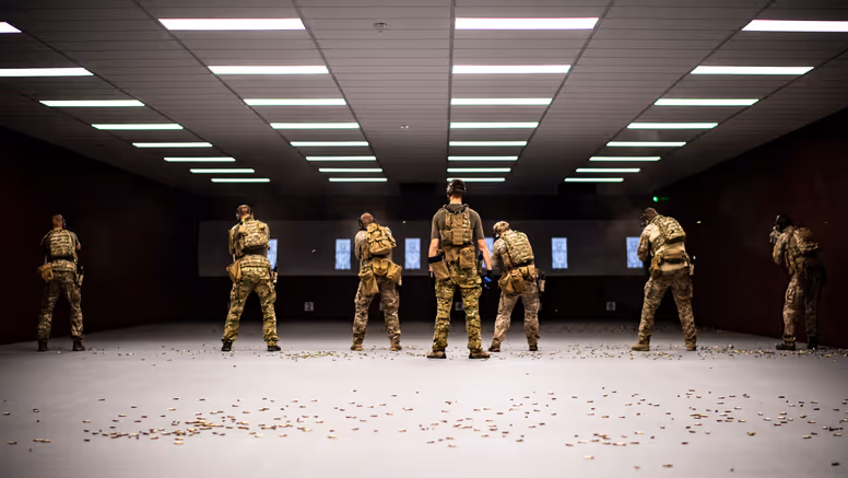 Zes militairen van het KCT, naast elkaar op een overdekte schietbaan. Achter hen ligt de vloer bezaaid met hulzen.