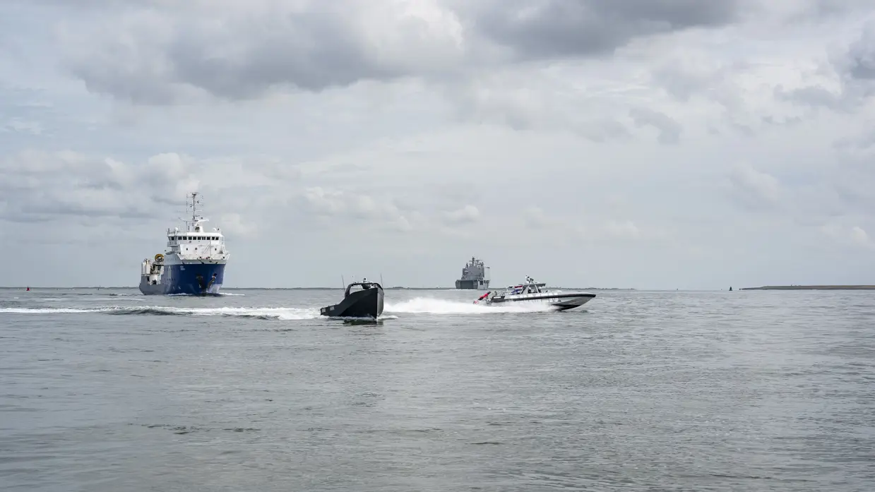 Twee kleine vaartuigen en twee grote schepen varen in formatie.