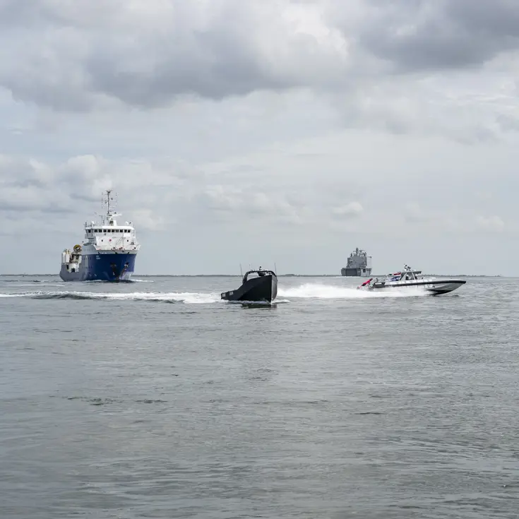 Twee kleine vaartuigen en twee grote schepen varen in formatie.