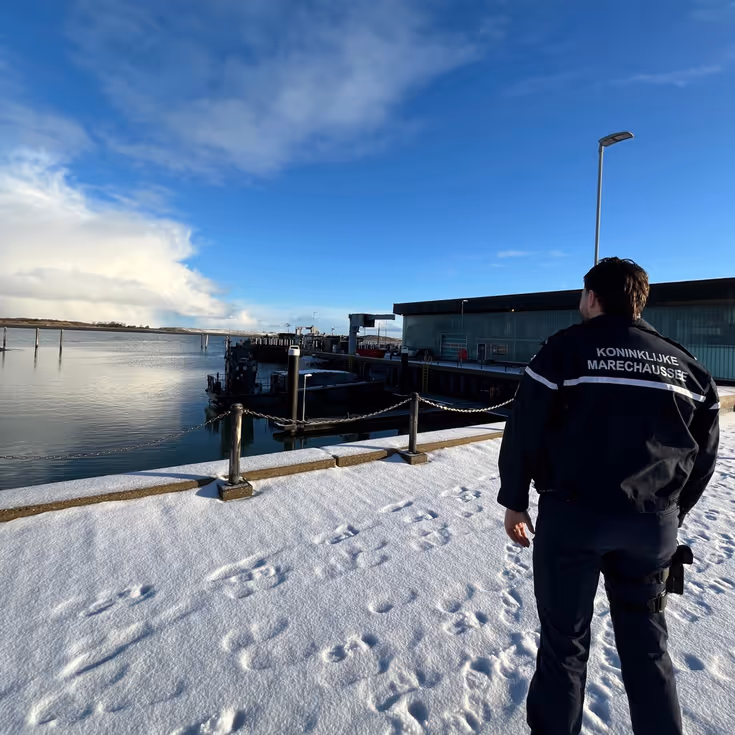 Marechaussee kijkt uit over besneeuwde haven.