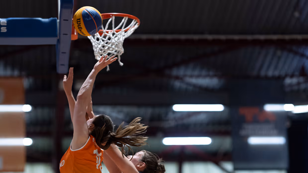 Een basketballer onder de basket in een sportzaal.