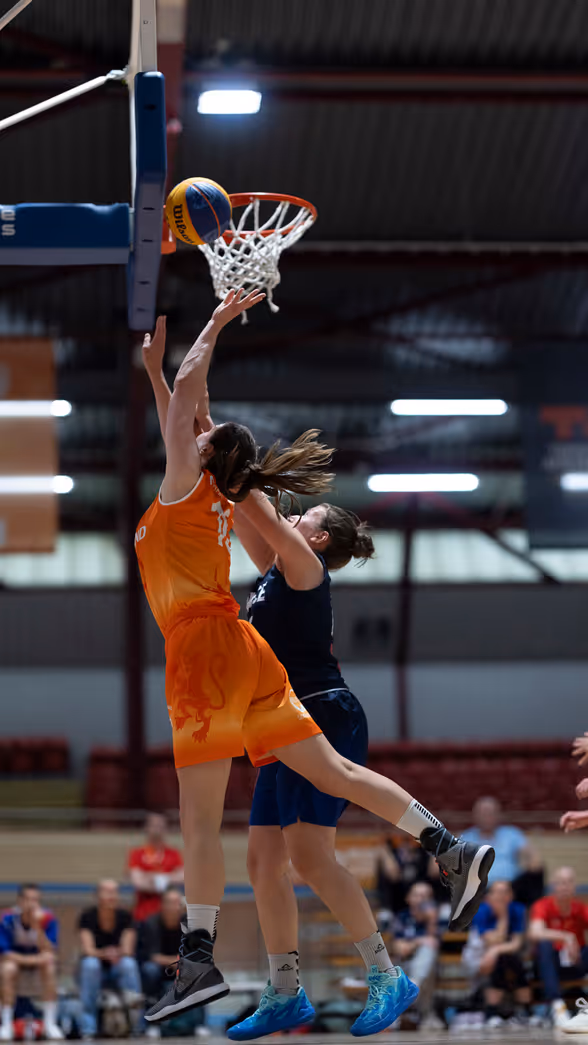 Een basketballer onder de basket in een sportzaal.