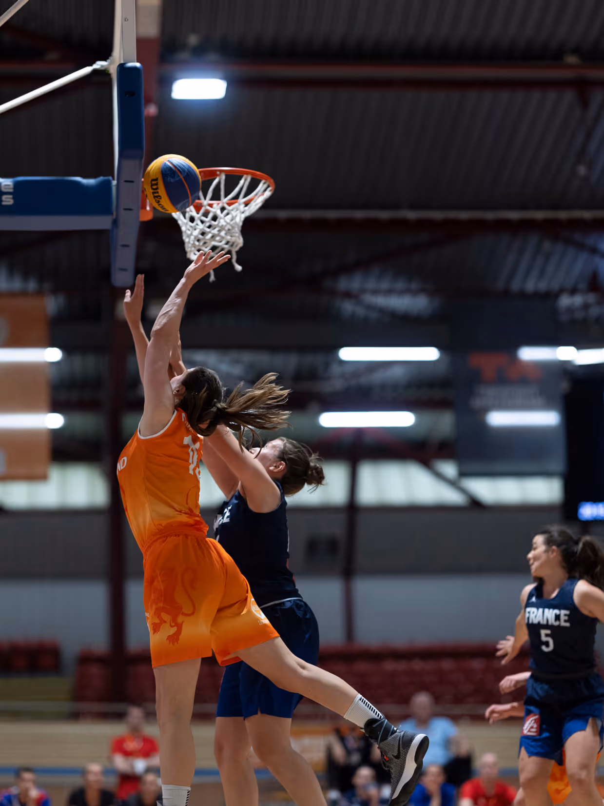 Een basketballer onder de basket in een sportzaal.