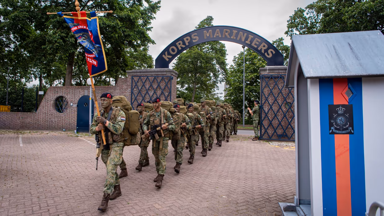 De geslaagden lopen achter hun vaandel de oude poort binnen van de Van Ghentkazerne. Rechts een wachthuisje.