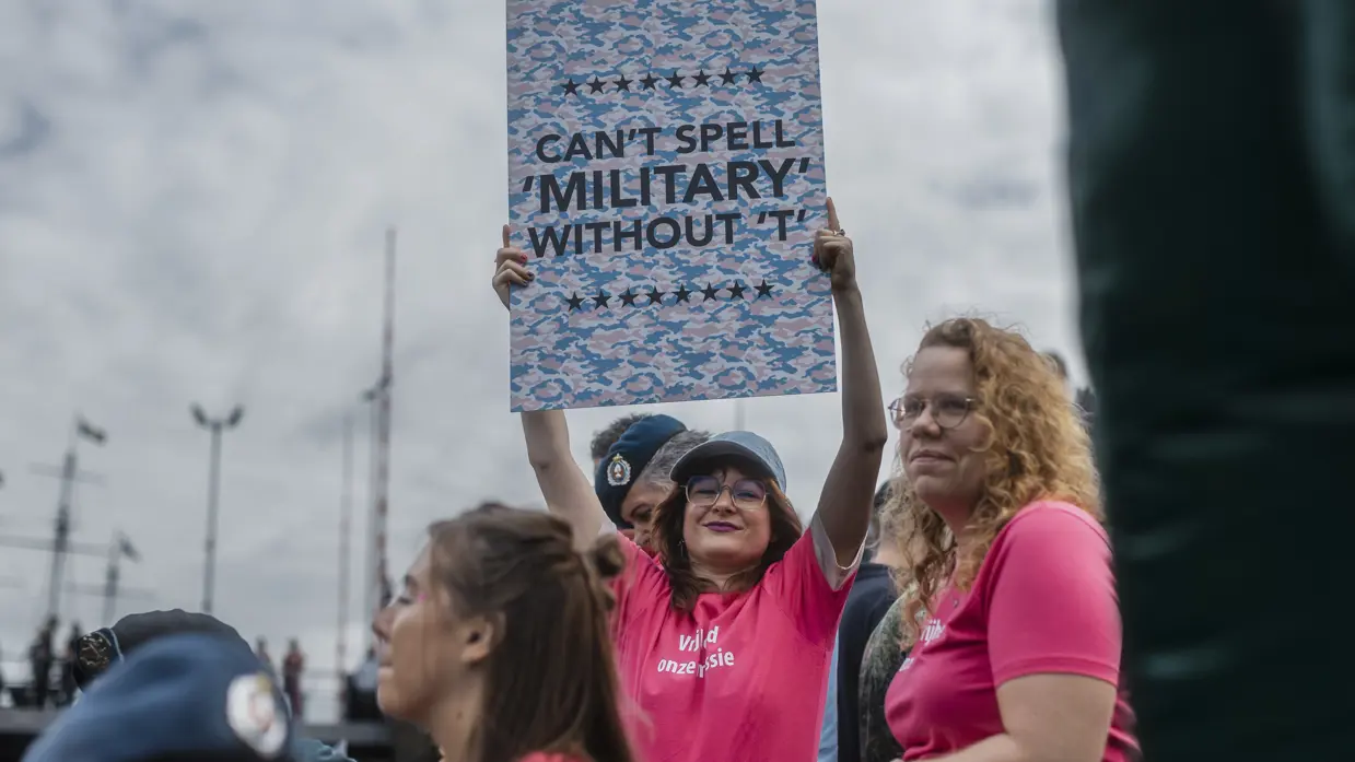 Een vrouw houdt een bord omhoog waarop staat: Can't spell 'military' without 'T'. 