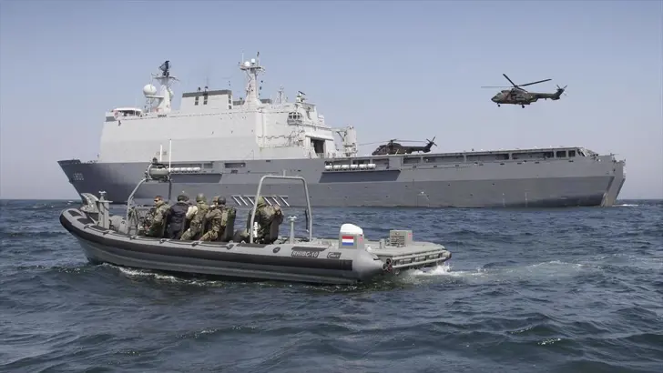 Amfibisch transportschip met snelle motorboot ervoor en helikopter erboven. 
