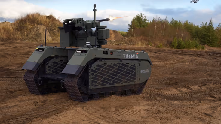 Een onbemand militair rupsvoertuig genaamd THEMIS met een kanon schiet op een zanderig terrein, terwijl een drone boven vliegt in een open landschap. 