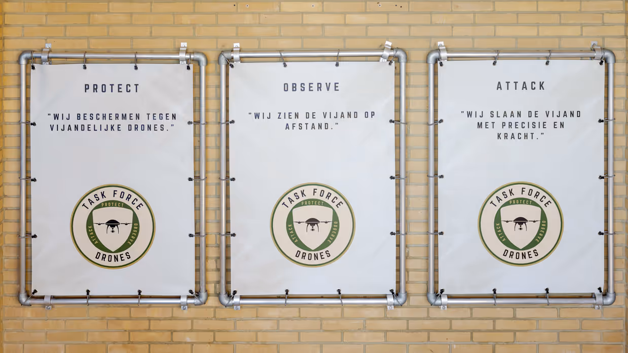Logo Task Force Drones wordt onthuld en borden met protect, observe en attack; hun motto.