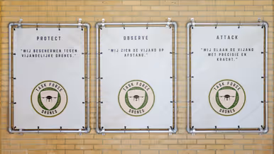 Logo Task Force Drones wordt onthuld en borden met protect, observe en attack; hun motto.