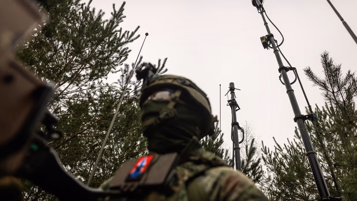 Gemaskerde militair in het veld met antennes op de achtergrond
