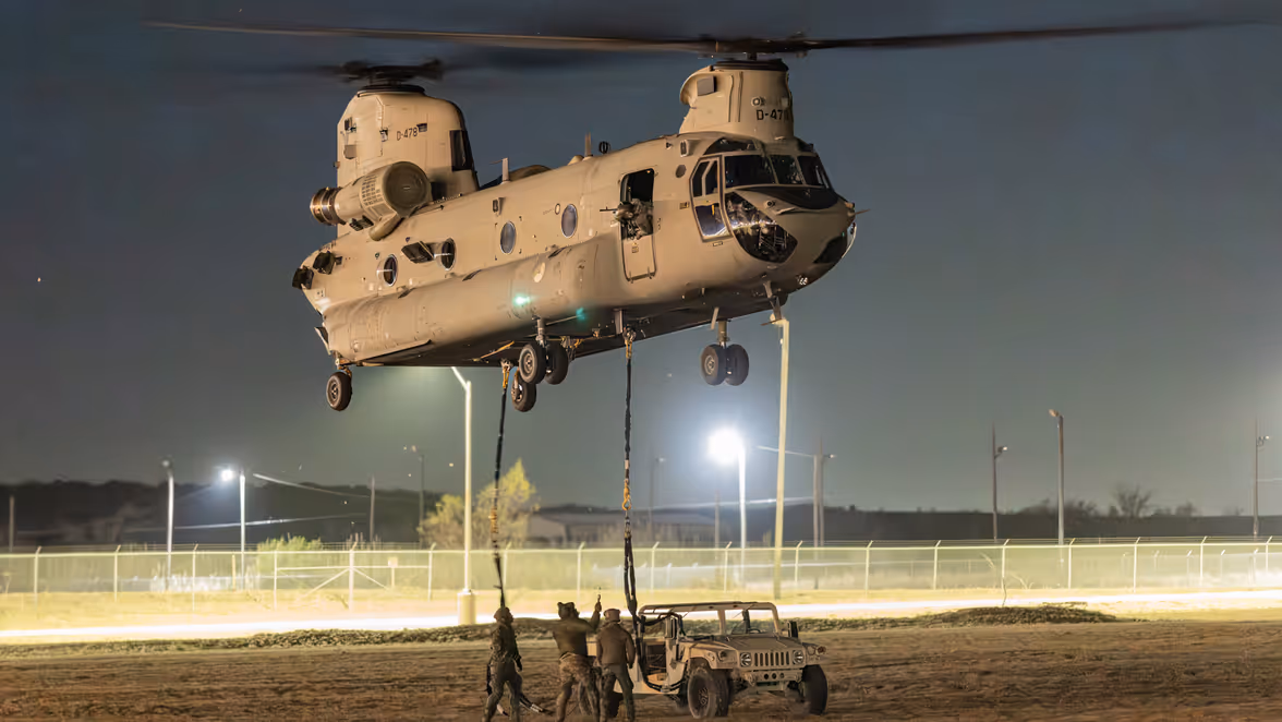 Alt-tekst: Bij duisternis koppelen militairen een voertuig aan als slingload onder een Chinook.  