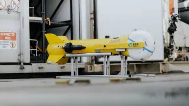  Een gele, raketvormige drone met voorop een witte bol. Deze is ook te zien achterop het varende bootje.