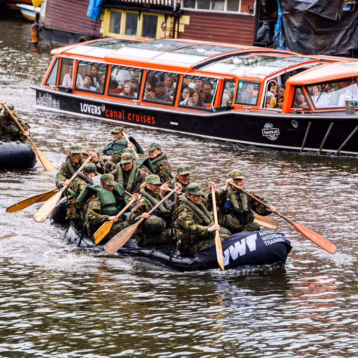 De deelnemers aan de NWT roeien in rubberboten door Amsterdam.