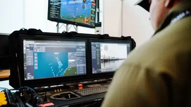 Een man zit achter een drietal schermen waarop onder meer de zee te zien is.