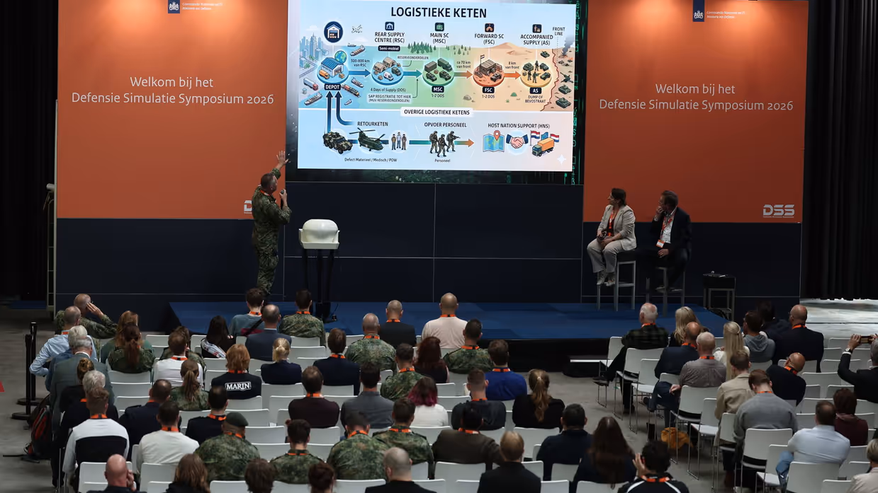 Een militair op een podium geeft een presentatie.